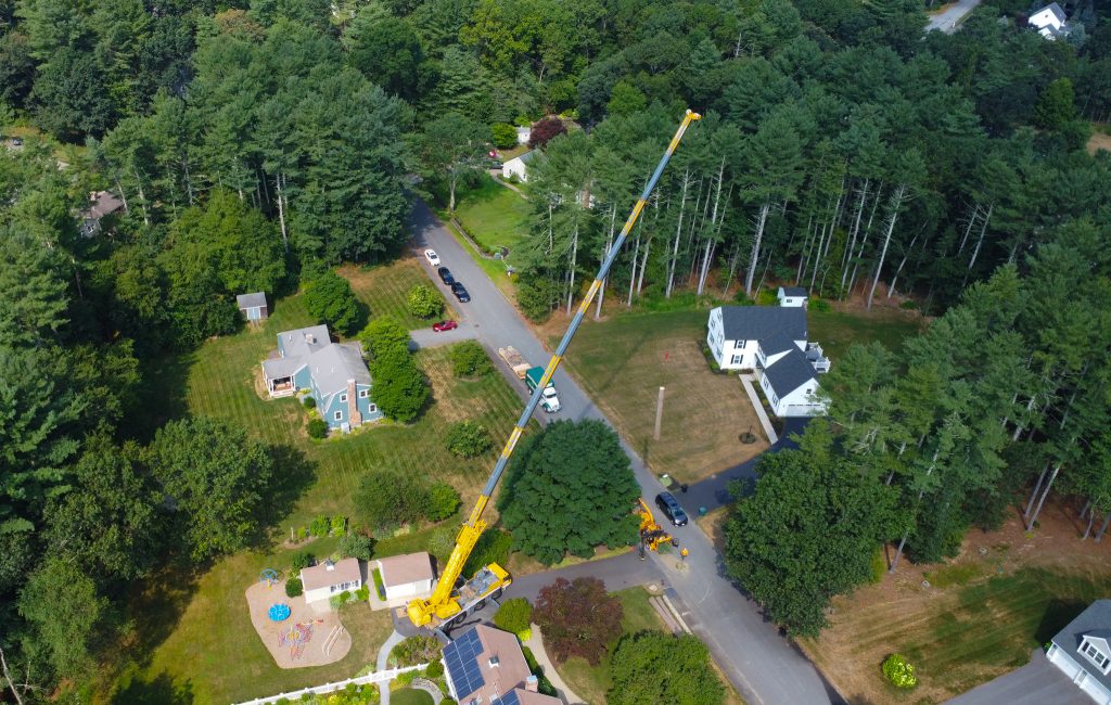 Crane reaching over to remove a tree in a residential area