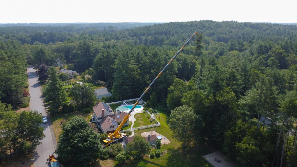 Crane reaching over to remove tree from a backyard